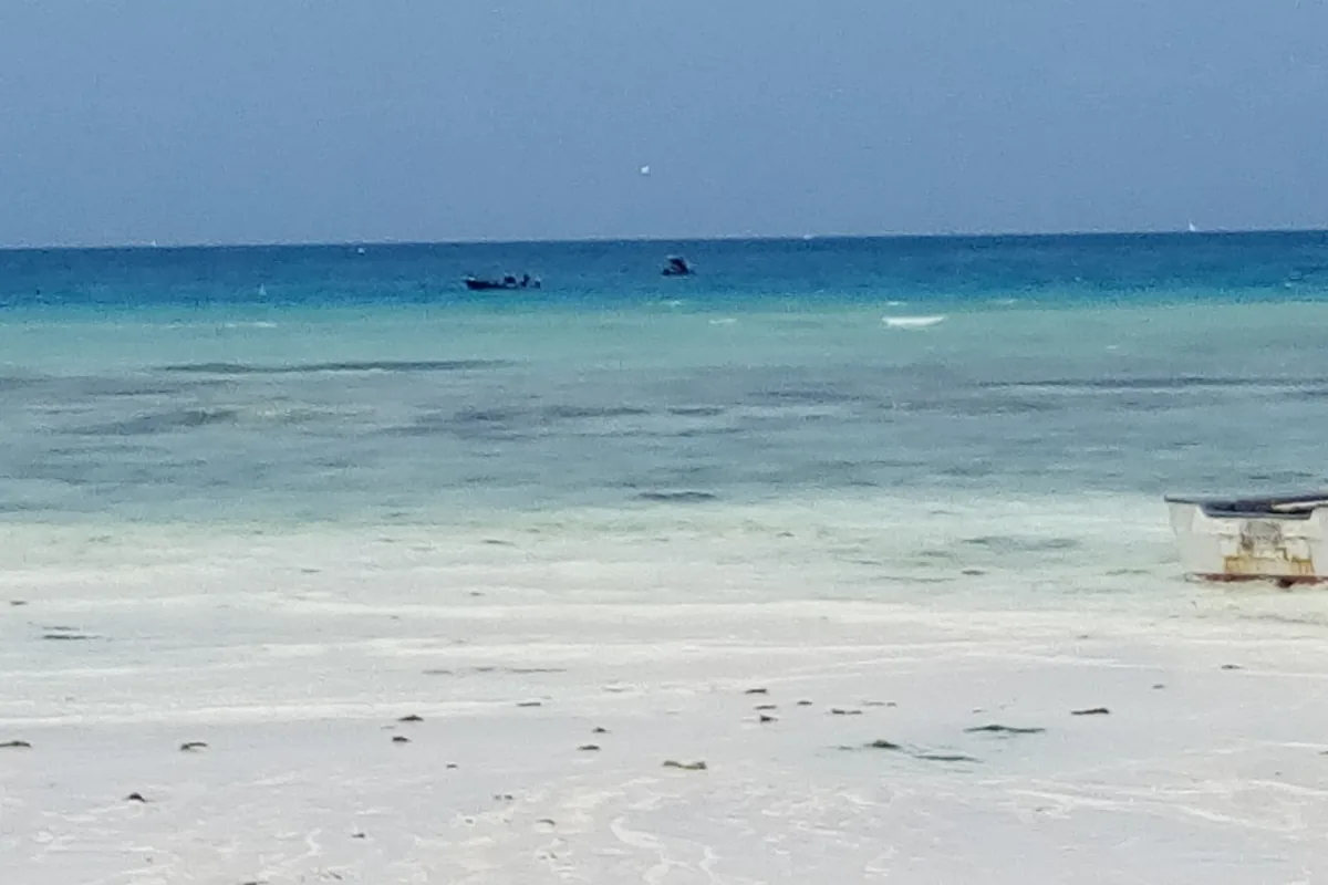 Bílopísčitá pláž v Nungwi na severním pobřeží Zanzibaru, s čistou mělkou vodou a lodí daleko na obzoru